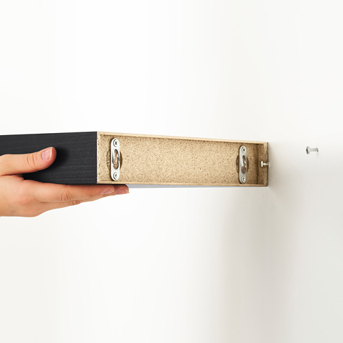 Estante de pared LACK sosteniendo con la mano, mostrando soportes de montaje ocultos. Diseño compacto que ahorra espacio.