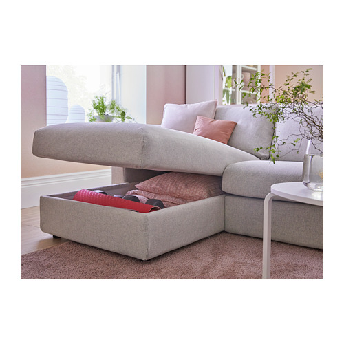 Moderno sofá gris con espacio de almacenamiento, almohadas rosas y rojas sobre suelo de madera clara.