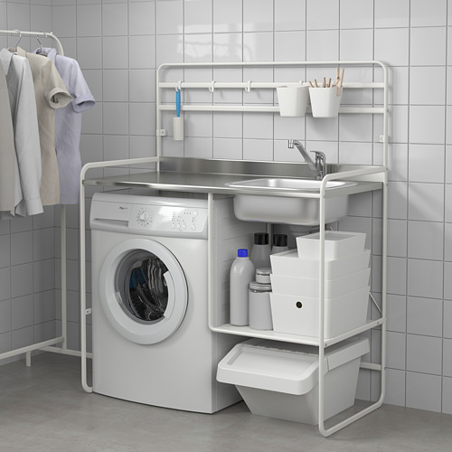 Moderna configuración de lavandería con una lavadora blanca debajo de una encimera de metal con fregadero, contenedores de almacenamiento y espacio para colgar la ropa.