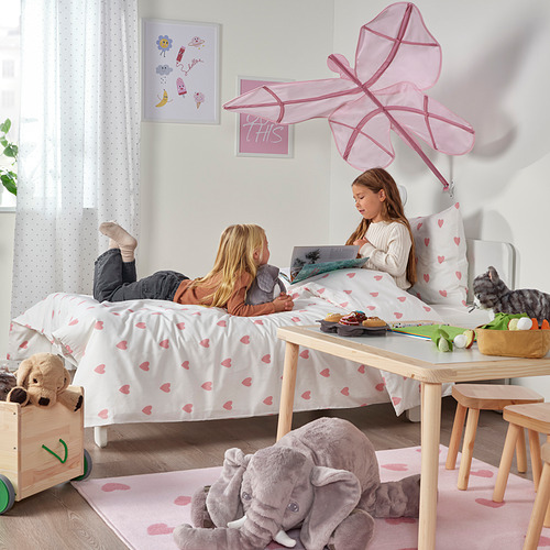 Habitación para niños con dos niñas en una alfombra de corazón jugando, rodeadas de peluches, incluido un gran peluche de elefante.