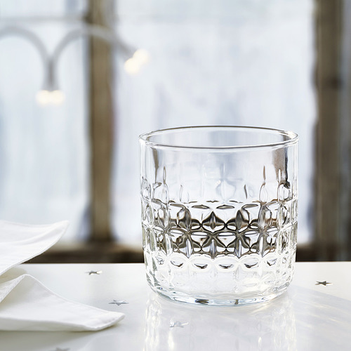 Taza de vidrio con patrones geométricos en relieve sobre mesa blanca, servilletas festivas y decoraciones de estrellas.