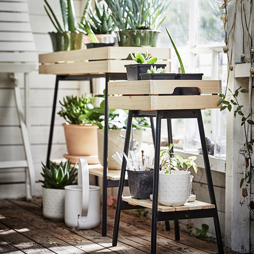 Plantas en cajas de madera con patas de metal, interior, hojas verdes, madera clara, acentos negros.