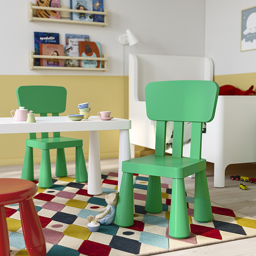 Pequeña y colorida área de juegos para niños con sillas MAMMUT verdes, mesa blanca y configuración de juguetes sobre una alfombra a cuadros.