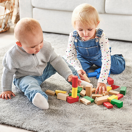 Dos niños pequeños juegan con bloques de madera sobre una alfombra. Construyen y apilan bloques de colores, promoviendo formas, colores y habilidades motoras.