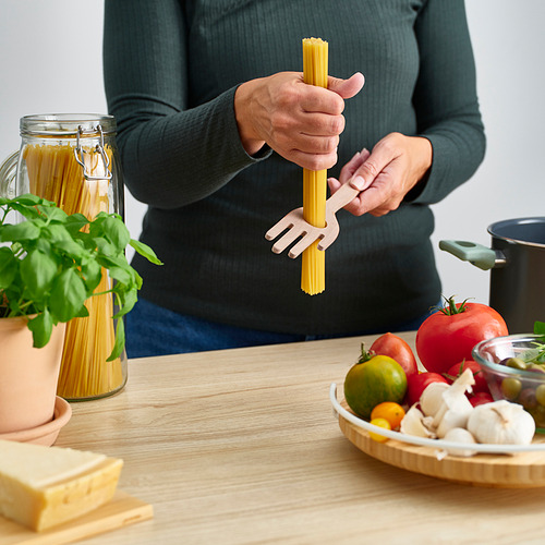 Persona sosteniendo un servidor de espaguetis sobre la mesa con ingredientes.