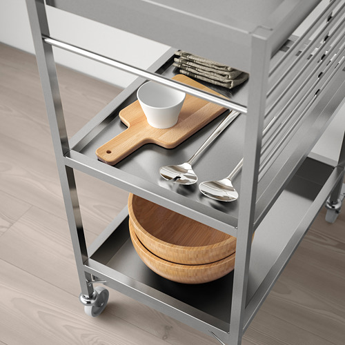 Moderno carro de cocina de acero inoxidable con ruedas, con utensilios, tabla de cortar y tazones, perfecto para la preparación de alimentos en espacios pequeños.
