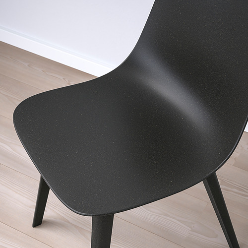 Silla negra con asiento y respaldo lisos y curvos sobre suelo de madera clara. Diseño moderno y minimalista con patas de apoyo a la vista.