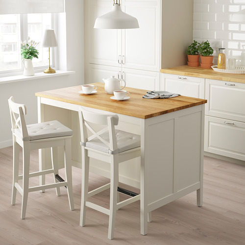 Pequeña isla de cocina blanca con encimera de roble, dos taburetes, en cocina luminosa.