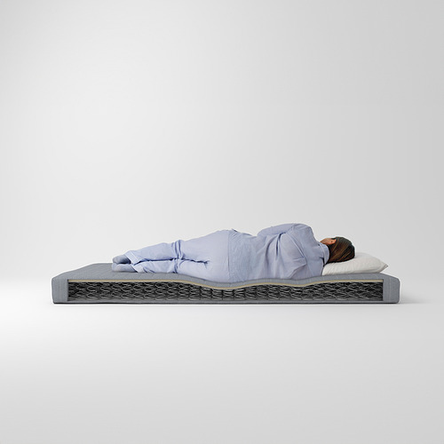 Persona durmiendo en un colchón VADSÖ gris, pijama azul claro, almohada blanca.