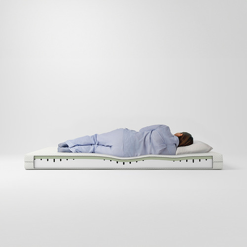 Persona durmiendo en un colchón de espuma viscoelástica ÅBYGDA azul claro, blanco con capa verde.