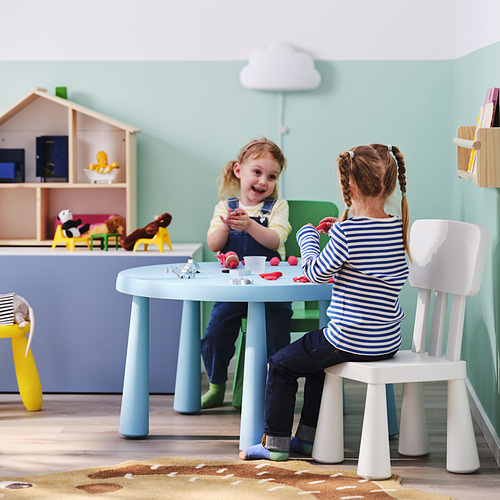 Niños jugando con juguetes en la mesa azul, cocina en el fondo.