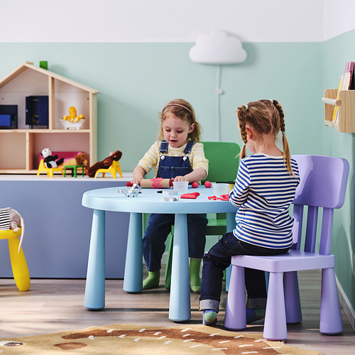 Dos niñas sentadas en una mesa infantil de colores pastel jugando con juguetes, rodeadas de muebles coloridos en una vibrante sala de juegos.