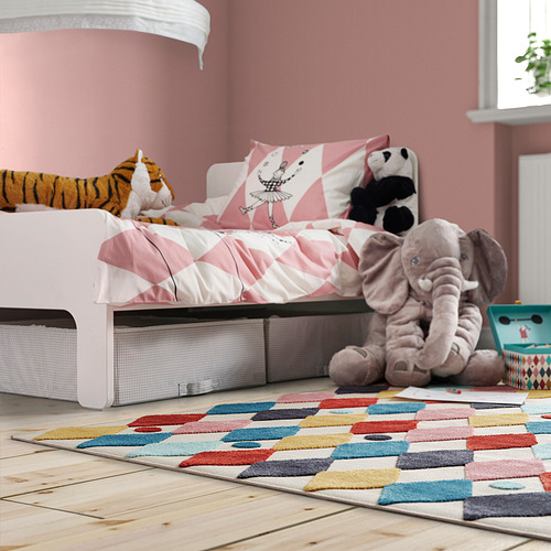 Habitación para niños con alfombra BUSENKEL, colorido patrón de arlequín, suave y duradero, cabe debajo de la cama, rodeado de juguetes de peluche, paredes rosas.