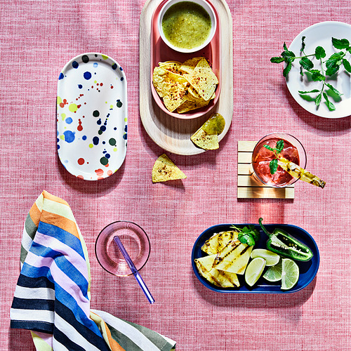 Coloridos platos RÖDSNULTRA de IKEA con patrones colocados en una mesa con bocadillos y bebidas.