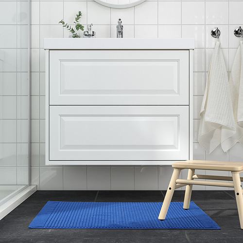 Baño moderno con alfombra de baño azul en contraste con el suelo oscuro.