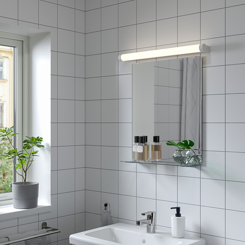 Elegante espejo NYSJÖN en pared de azulejos, con lavabo y estante debajo de una ventana soleada.