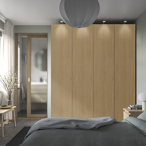 Dormitorio moderno con gran armario PAX de madera clara, ropa de cama gris suave, lámpara colgante redonda y lámpara de recipiente blanca sobre mesita de noche de madera.
