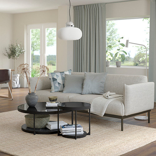 Luminoso salón con grandes ventanales, un sofá FRÖTORP beige, mesa de centro negra, lámpara colgante blanca, cortinas grises y plantas.