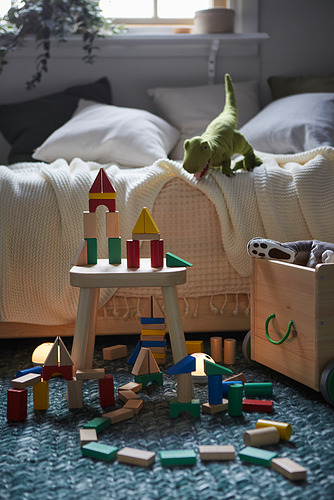 Acogedora área de juegos para niños, coloridos bloques de madera sobre la mesa, dinosaurio de juguete cerca de la cama, alfombra azul.