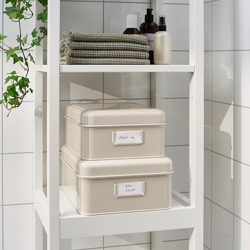 Cajas de almacenamiento de metal blanco con etiquetas, maquillaje y aromas de spa en los estantes del baño.