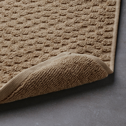 Alfombrilla de baño beige con superficie de algodón texturizado, alta absorción, borde doblado.