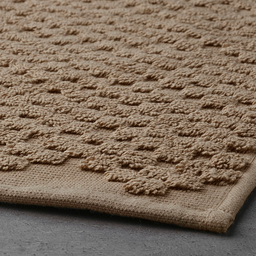 Alfombrilla de baño de algodón beige, texturizada, de alta calidad, con un patrón intrincado y una superficie de rizo suave, que proporciona comodidad y alta absorción.