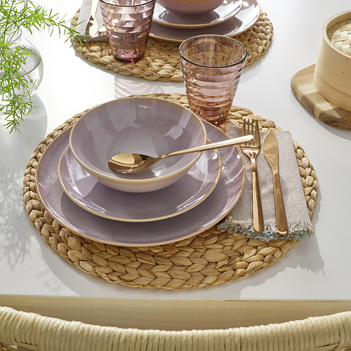 Mesa con platos, cuencos, cubiertos dorados, manteles individuales tejidos, vasos y vegetación.
