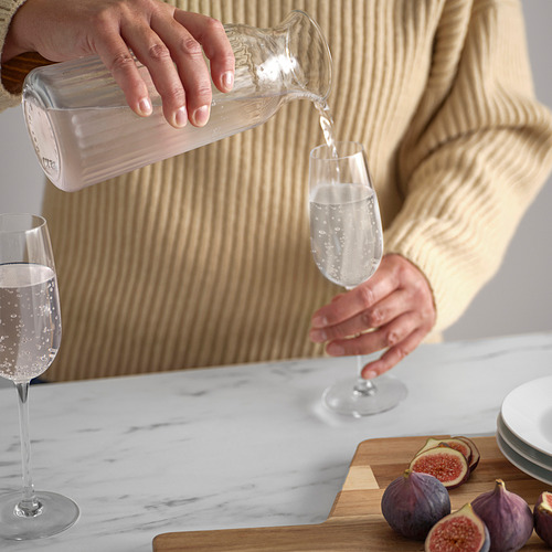Persona vertiendo agua de una jarra de vidrio transparente en una copa de vino, mostrando la versatilidad de la cristalería VARDAGEN para servir bebidas.