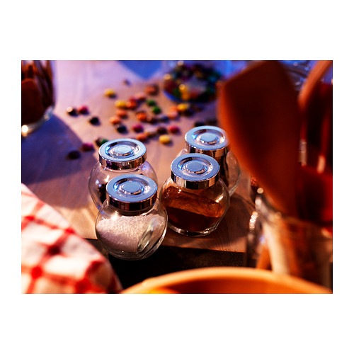 Cuatro frascos de vidrio transparente con tapas metálicas sobre una mesa junto a caramelos de colores.