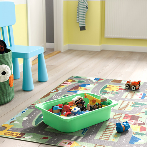 Juguetes y recipientes para niños en una alfombra de juego. El contenedor verde contiene una variedad de figuras de acción y vehículos. La silla azul y la cesta de juguetes están cerca.