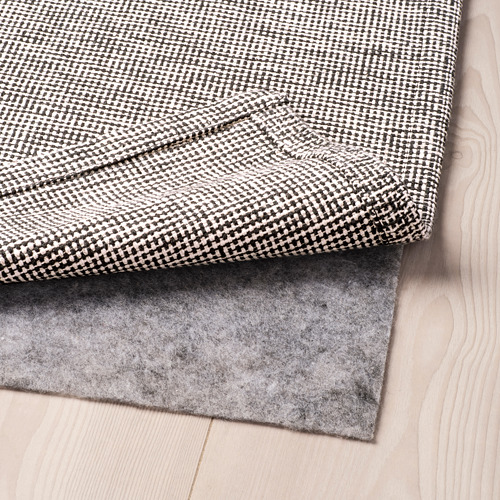 Alfombra sobre suelo de madera clara, reveladora capa de alfombra debajo. Características de las pantallas lavables a máquina, fáciles de limpiar y aptas para muchas habitaciones.