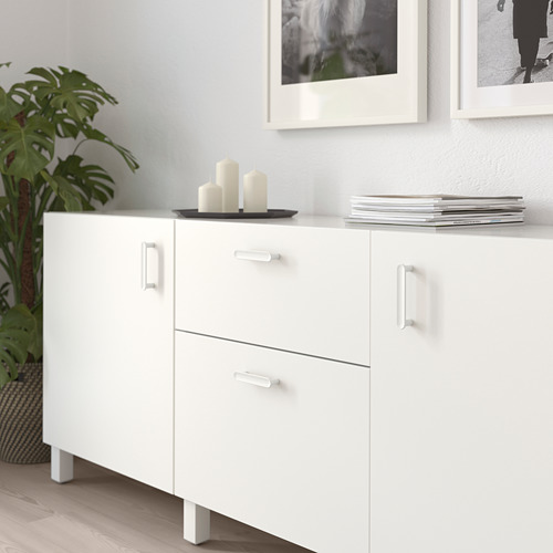 Mueble blanco con tres cajones y dos puertas, adornado con velas y plantas, que ofrece espacio de almacenaje y decoración.