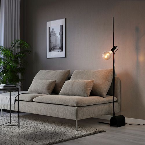 Salón minimalista con lámpara gris, sofá beige, mesa auxiliar negra y foto de pared.