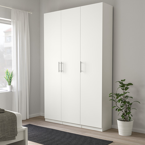 Gran armario blanco cerca de la ventana con cortinas, alfombra gris y dos plantas en macetas. Diseño sin asa con superficies lisas.
