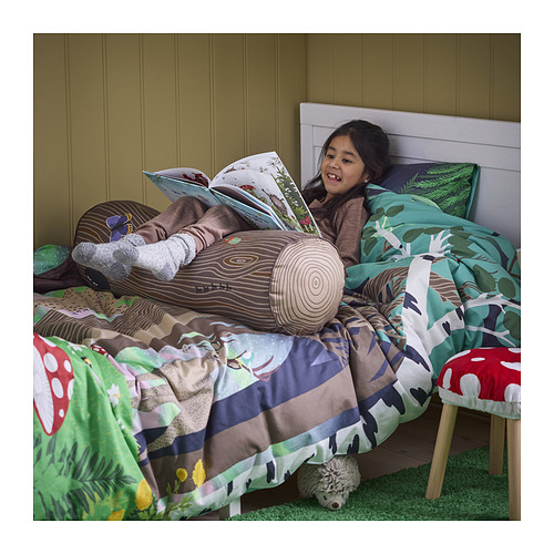 Un niño en la cama con almohadas de temática forestal, leyendo. Las almohadas sostienen su espalda y cabeza, asemejándose a troncos de árboles con insectos rastreros.