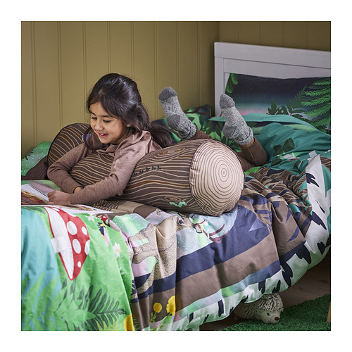 La niña lee en la cama con la almohada de apoyo SKOGSDUVA. El cojín en forma de tronco de árbol ayuda a la comodidad.