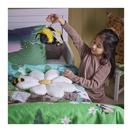 La niña juega con un juguete de abeja suave en la cama, sosteniéndolo por un bucle, promoviendo el juego imaginativo y la conciencia del bosque.