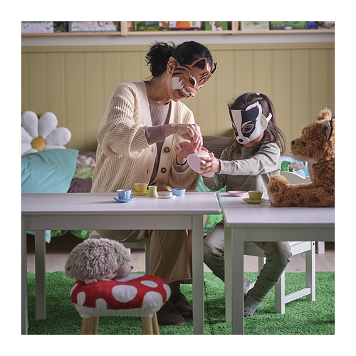 Un adulto y un niño jugando con máscaras SKOGSDUVA, sentados en una pequeña mesa con tazas de té, rodeados de peluches de juguete.