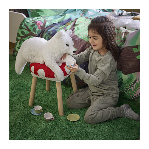 Una niña juega al té con un zorro ártico de peluche en un taburete, usando mini tazas y un platillo. El zorro es blanco con patas esponjosas y ojos bordados.