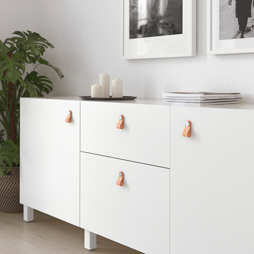 Mueble blanco con manijas de cuero; Tres cajones, un estante superior con velas y revistas.