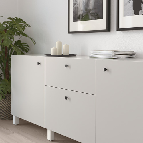 Mueble blanco con tiradores HACKÅS negros; sostiene velas, libros y plantas.
