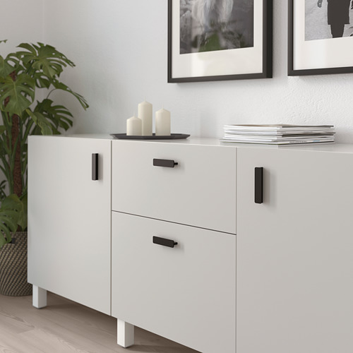 Mueble blanco con tiradores negros, acabado liso. La parte superior sostiene velas, la parte inferior tiene cajones.