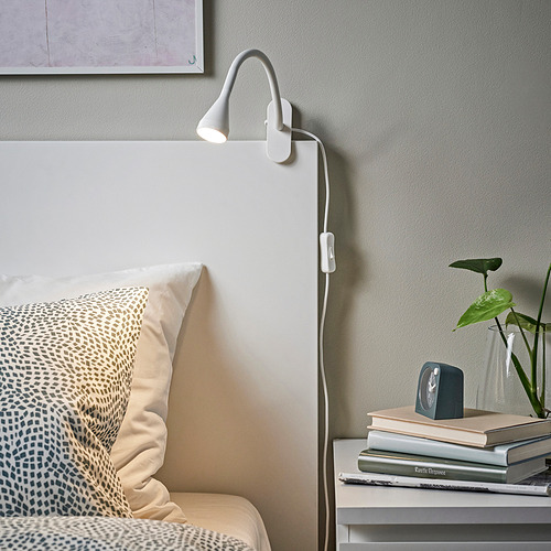 Lámpara blanca NÄVLINGE al lado de la cama, luz focalizada, planta, libros.
