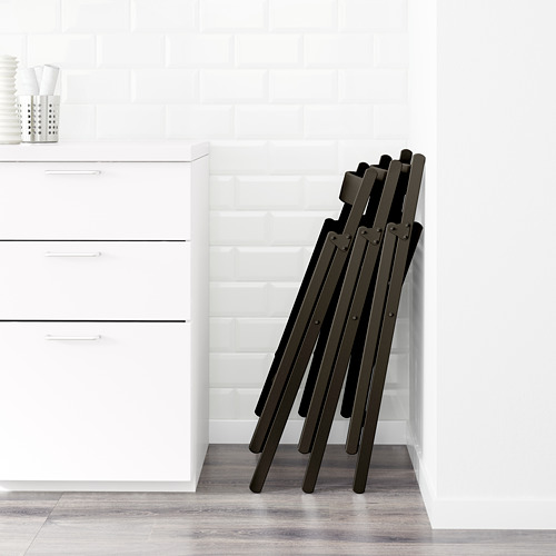 Las sillas oscuras plegables se apoyan contra una pared blanca, ideales para ahorrar espacio en la cocina o el comedor.