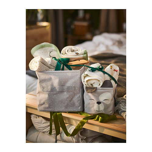 Dos cajas de almacenamiento de tela con diseños de osos y lunares en un estante de madera, que contienen artículos para bebés como pañales, chupetes, ropa y juguetes.