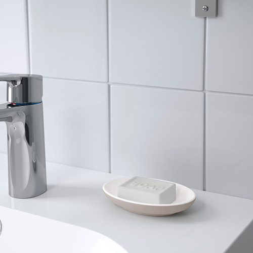 Jabonera ovalada blanca sobre la encimera de un baño, sosteniendo una pastilla de jabón, junto a un grifo cromado brillante. Forma parte de la serie EKOLN.