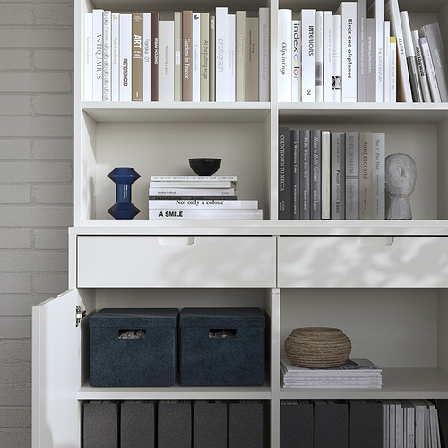 Estantería blanca con cajas de almacenamiento grises y artículos decorativos, con un diseño limpio.