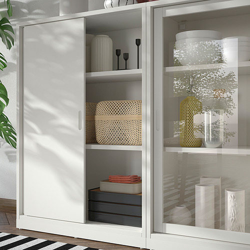 White TONSTAD storage unit with sliding doors and glass doors, featuring woven baskets, vases, and boxes. Modern, off-white design with clean lines.