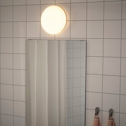 Una lámpara de techo moderna emite una luz suave y uniforme en un baño con azulejos, perfecta para iluminar el espacio.