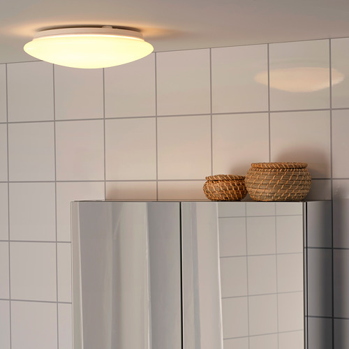La luz brillante del techo ilumina el baño con azulejos modernos; Cestas de mimbre en un elegante soporte junto a un gabinete brillante.